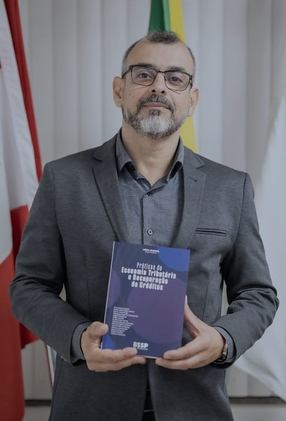 Guilherme de Almeida Corrêa de pé, de paletó cinza, segurando o livro do qual é coautor, no lançamento em Florianópolis